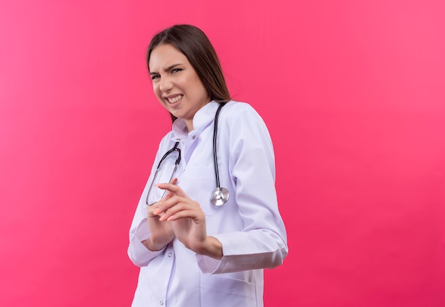 Jovem médica enjoada usando estetoscópio bata médica em fundo rosa isolado