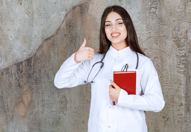 Jovem médica gesticulando com o polegar enquanto segura o livro