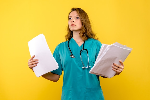 Jovem médica segurando arquivos no espaço amarelo de frente