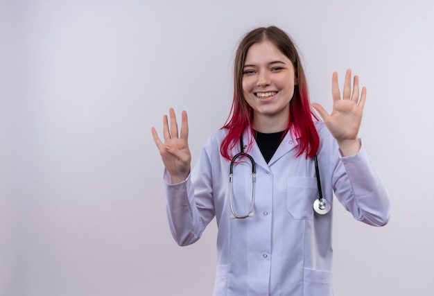 Jovem médica sorridente usando um manto médico de estetoscópio mostrando diferentes números em um fundo branco isolado com espaço de cópia