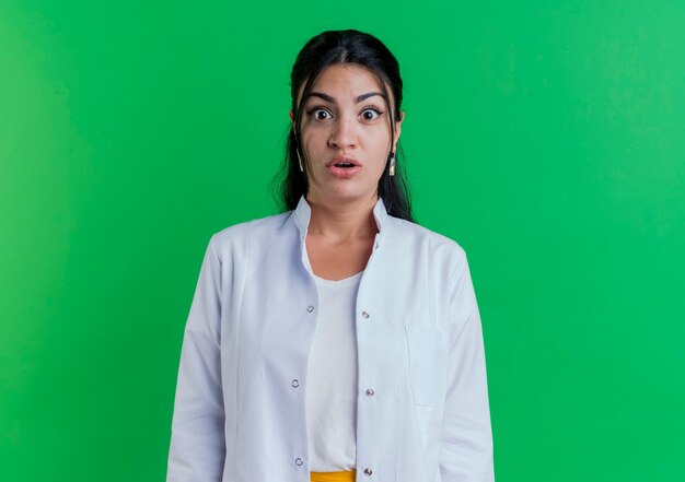 Jovem médica surpreendida usando túnica médica isolada em uma parede verde com espaço de cópia