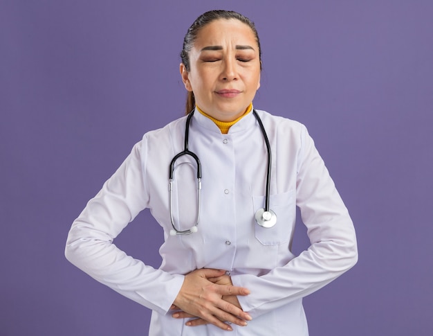 Jovem médica tocando a barriga parecendo indisposta e sentindo dor