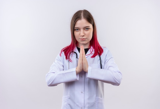 Foto grátis jovem médica usando estetoscópio manto médico mostrando gesto de orar na parede branca isolada