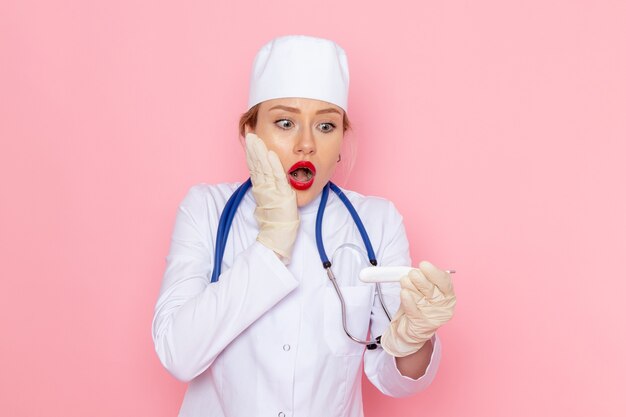 Jovem médica vestida de terno médico branco com estetoscópio azul segurando o dispositivo no trabalho do hospital médico de medicina espacial rosa