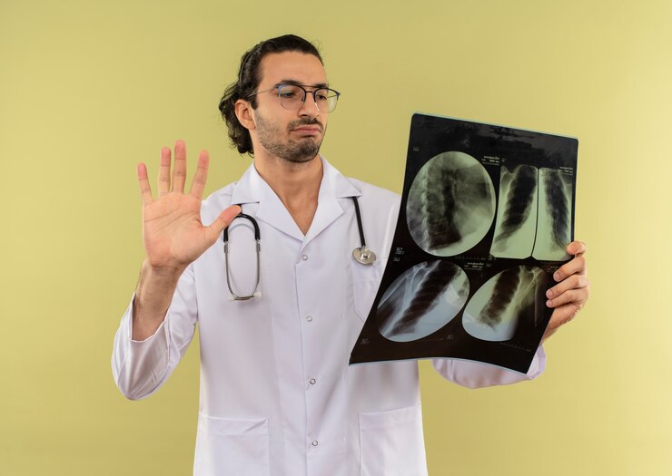 Foto grátis jovem médico a pensar com óculos ópticos, vestindo túnica branca com estetoscópio segurando e olhando para o raio-x mostrando gesto de parada no verde