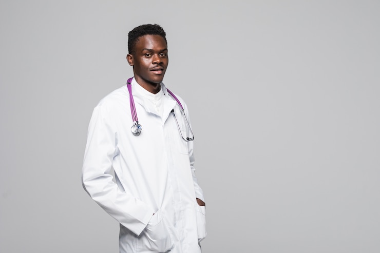 Foto grátis jovem médico afro-americano em uniforme branco, isolado no fundo branco em pé com os braços no olhando olhando profissional e altamente competente no campo da especialização médica