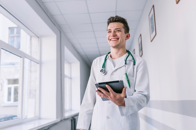 Jovem médico alegre com um comprimido no corredor