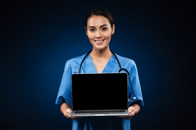 Jovem médico alegre mostrando a tela em branco do computador portátil isolado
