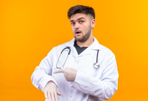 Jovem médico bonito usando um vestido branco médico, luvas médicas brancas e estetoscópio