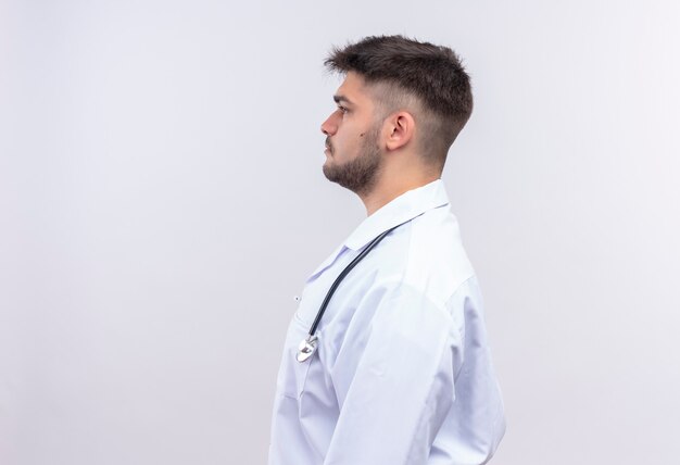 Jovem médico bonito usando um vestido branco médico, luvas médicas brancas e estetoscópio