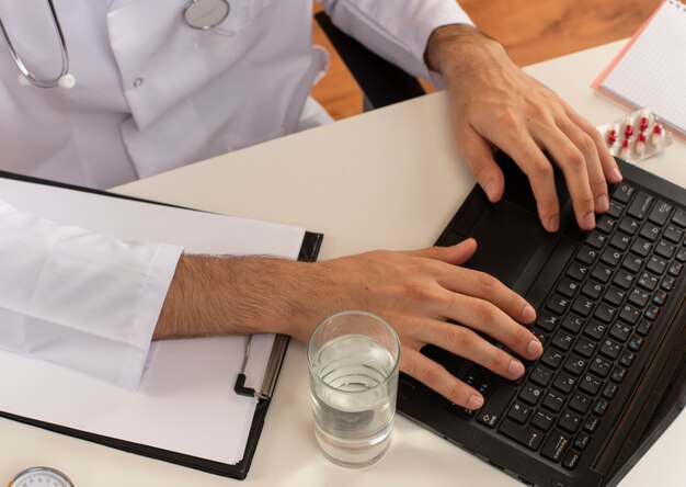 Jovem médico com óculos médicos, roupão médico e estetoscópio, sentado à mesa