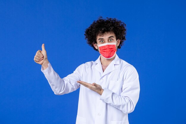 Jovem médico de frente para o terno médico com máscara vermelha sobre azul
