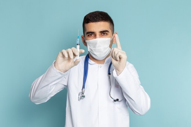 Jovem médico de terno branco com estetoscópio azul segurando injeção