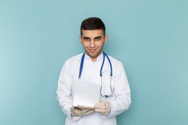 Jovem médico de terno branco com estetoscópio azul segurando o bloco de notas e sorrindo
