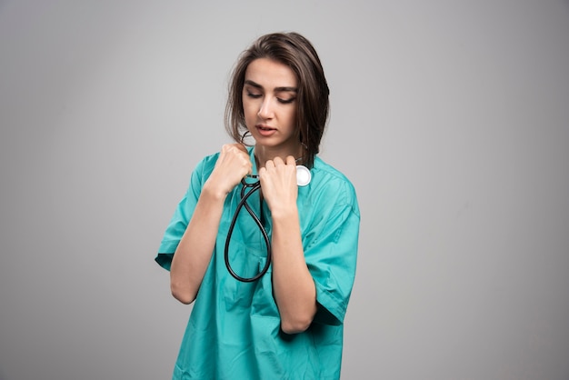 Jovem médico de uniforme usando estetoscópio na parede cinza.