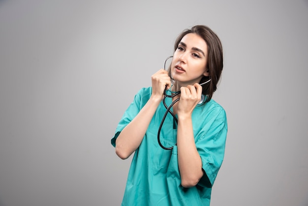 Jovem médico de uniforme usando estetoscópio na parede cinza.