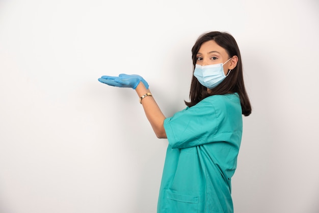 Jovem médico em máscara médica e luvas, abrindo as mãos no fundo branco.