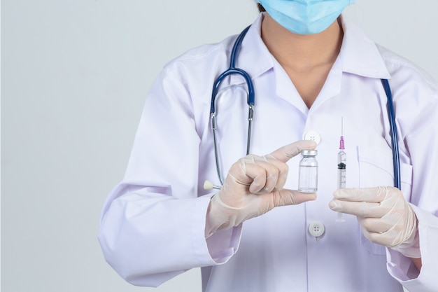 Jovem médico está segurando a seringa hipodérmica com luvas de borracha do frasco de vacina na parede cinza.