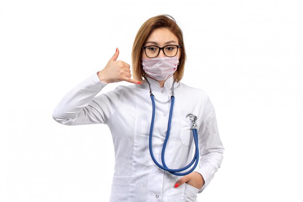 jovem médico feminino em traje médico branco com estetoscópio em máscara protetora branca posando em branco