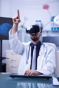 Jovem médico masculino com fone de ouvido de realidade virtual apontando. tecnologia futura em hospitais.