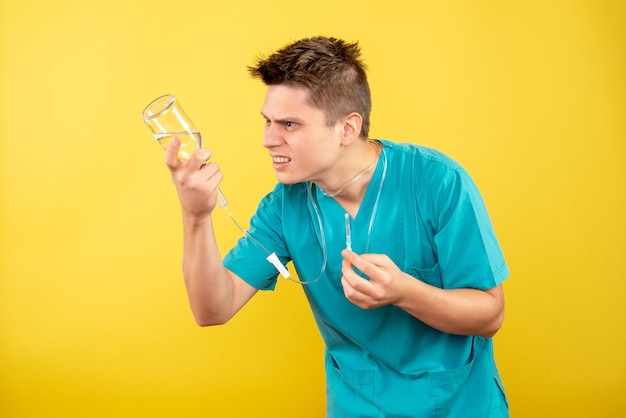 Jovem médico masculino em terno médico segurando um conta-gotas em fundo amarelo de vista frontal