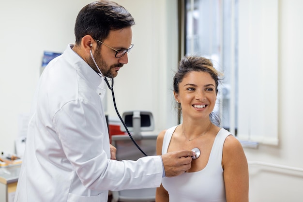 Jovem médico ouve o peito do coração do paciente feminino com estetoscópio na reunião clínica Man GP checkup examina cliente mulher com conceito de saúde phonendoscope