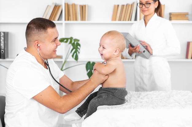 Jovem médico ouvindo bebê adorável com estetoscópio