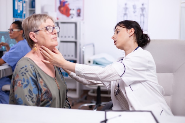 Jovem médico palpando o pescoço de uma mulher idosa, paciente idoso, visitando o médico no hospital, verificando a garganta da tireoide, tocando a saúde na clínica. especialista em saúde, medicare, conceito médico de tratamento.