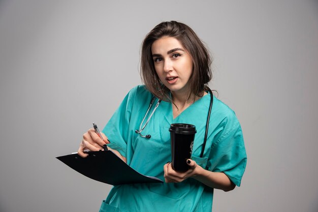 Jovem médico segurando a xícara e a área de transferência em fundo cinza. Foto de alta qualidade