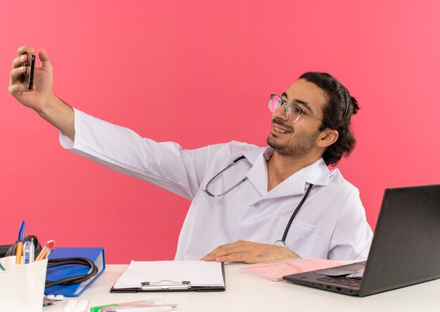 Jovem médico sorridente com óculos médicos e roupão médico com estetoscópio