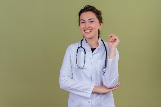 Jovem médico sorridente, vestindo jaleco médico e estetoscópio na parede verde