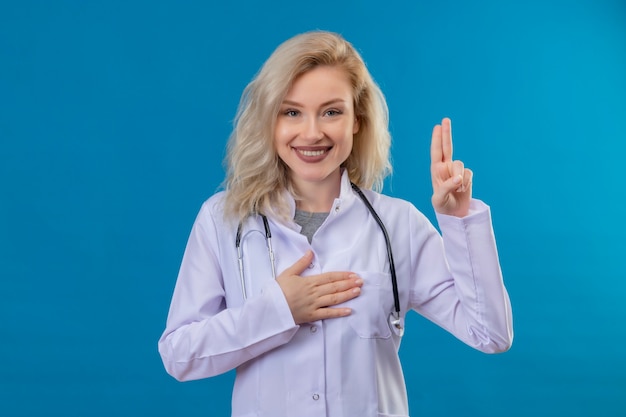 Jovem médico usando estetoscópio e vestido de médico - na parede azul