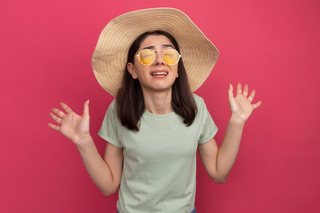 Foto grátis jovem menina bonita caucasiana irritada com chapéu de praia e óculos escuros, com as mãos vazias e os olhos fechados