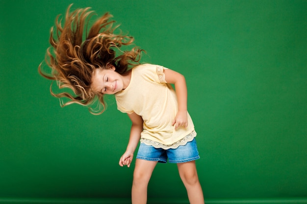 Jovem menina bonita dançando sobre parede verde