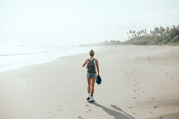 jovem menina linda posando na praia, oceano, ondas, sol brilhante e pele bronzeada