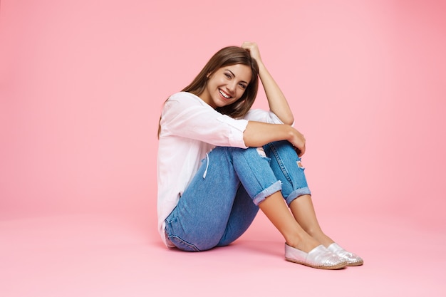 Jovem menina sorridente, sentada no chão, abraçando os joelhos, olhando em linha reta