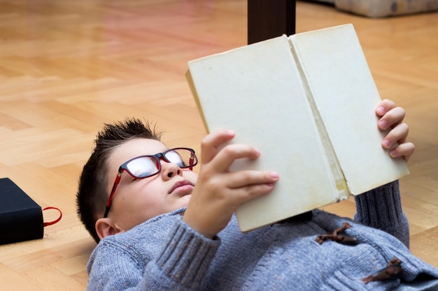 Jovem menino deitado no chão entre os livros e lendo um livro, menino estudando a lição de casa.