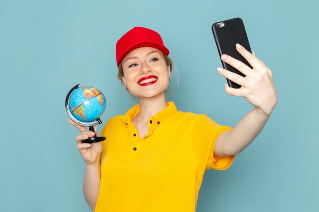 Jovem mensageira de frente para mulher de camisa amarela e capa vermelha tirando uma selfie com o globo no espaço azul