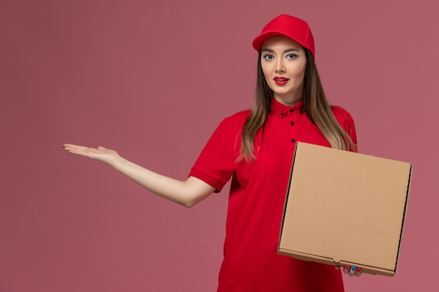 Jovem mensageira de uniforme vermelho segurando uma caixa de comida de entrega em fundo rosa claro.