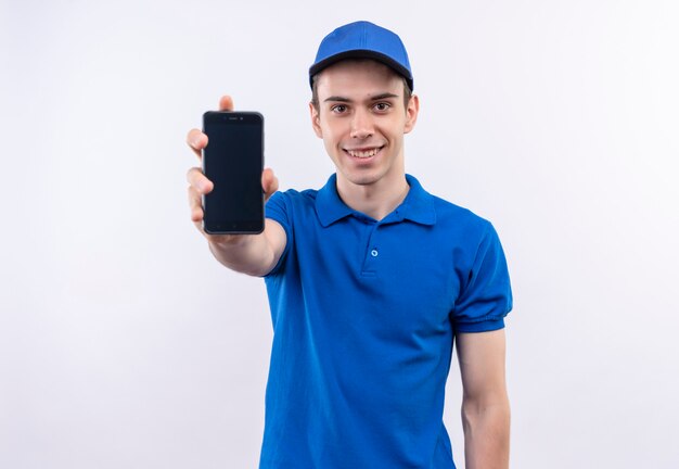 Jovem mensageiro de uniforme azul e boné azul, sorrindo e mostrando um telefone