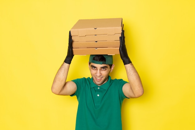 Foto grátis jovem mensageiro masculino com boné verde de camisa verde segurando caixas de entrega com sorriso amarelo