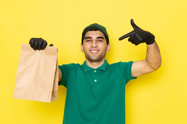 Jovem mensageiro masculino com boné verde de camisa verde segurando o pacote de entrega com um sorriso amarelo