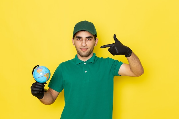 Jovem mensageiro masculino com boné verde e camisa verde segurando o globo terrestre com luvas pretas amarelas