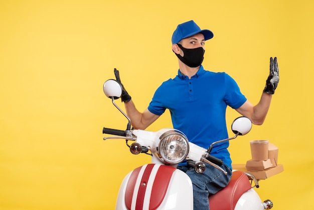 Foto grátis jovem mensageiro masculino de uniforme azul sobre fundo amarelo covid-job de entrega de pandemia de vírus trabalho de bicicleta de frente