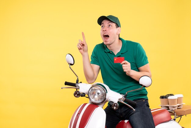 Jovem mensageiro masculino de uniforme verde segurando um cartão de banco vermelho sobre amarelo de frente