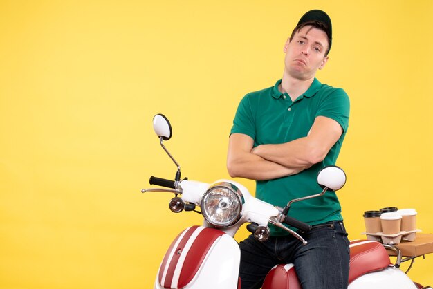 Jovem mensageiro masculino de uniforme verde, vista frontal, posando em bicicleta amarela
