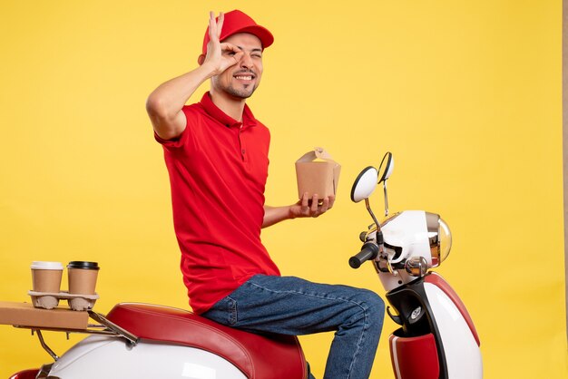 Jovem mensageiro masculino de uniforme vermelho com entrega de comida em fundo amarelo de frente