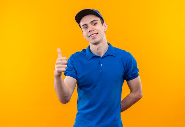 Jovem mensageiro vestindo uniforme azul e boné azul fazendo feliz sinal de positivo