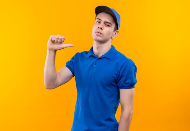 Jovem mensageiro vestindo uniforme azul e boné azul fazendo polegares sérios em si mesmo