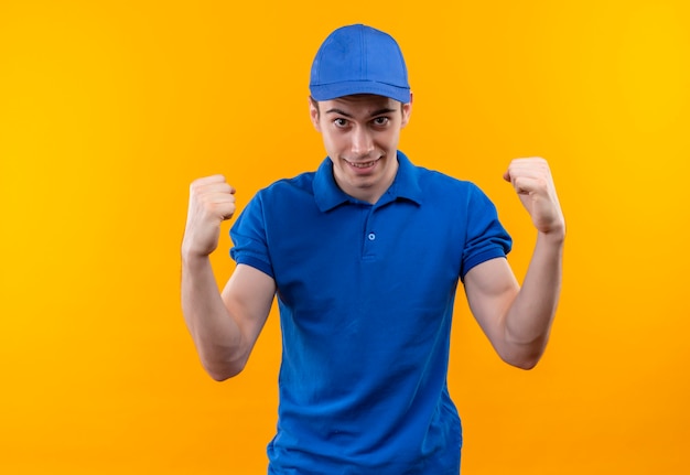 Foto grátis jovem mensageiro vestindo uniforme azul e boné azul fazendo punhos felizes